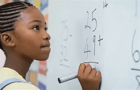 Learner solving two-digit addition on a classroom whiteboard for numeracy practice.