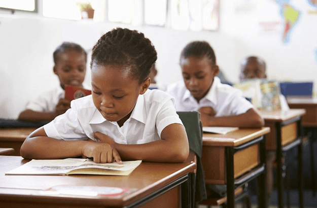 Learner concentrating on literacy work at a desk in a bright classroom.